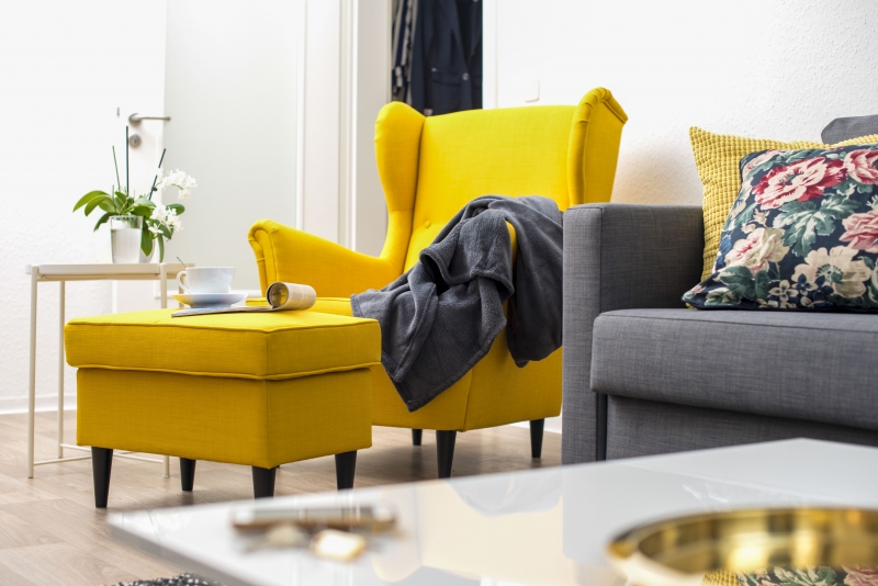 Ein modernes Wohnzimmer mit einem gelben Stuhl, einem grauen Sofa und einem Tisch mit einer Orchidee