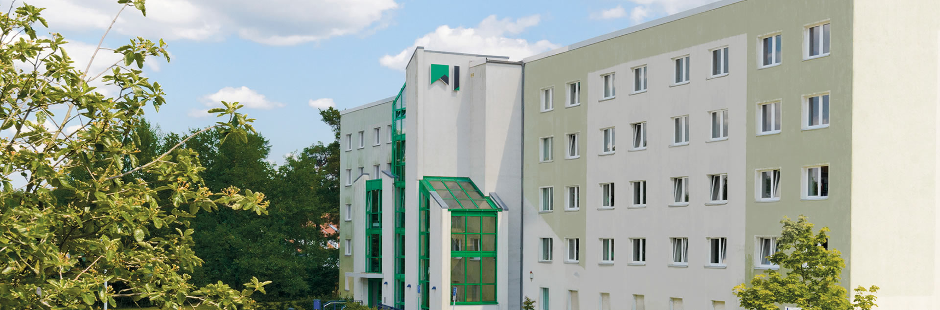 Ein weiß-grüner Wohnblock und davor stehen Bäume und Büsche